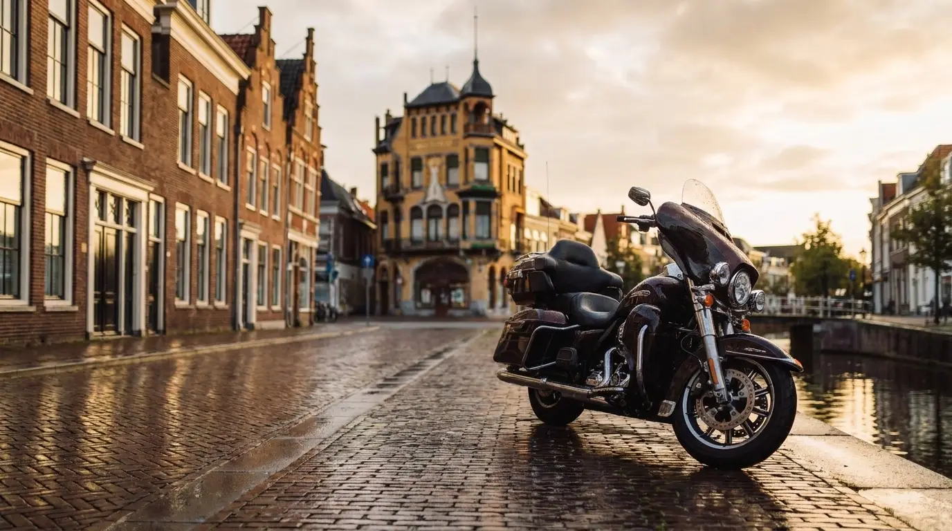 De Centraal Apotheek subtiel herkenbaar in de achtergrond. — Een sfeervolle, natgeregende klinkerstraat langs de gracht van de Nieuwestad in Leeuwarden. Historische trapgevels en oude bakstenen panden weerspiegelen in de glimmende, vochtige straatstenen. De motor staat stoer geparkeerd aan de kade.